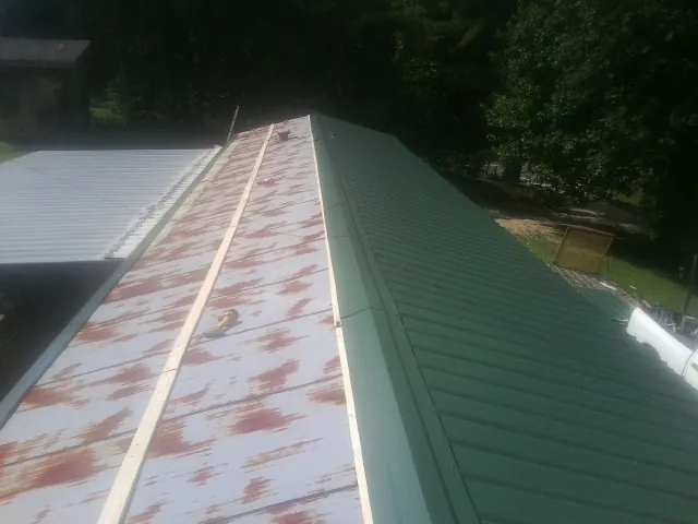 Old rusted panels beside newly installed green metal roofing — Wind Damage Roof Repair by Roofing Brothers in Dixon Springs