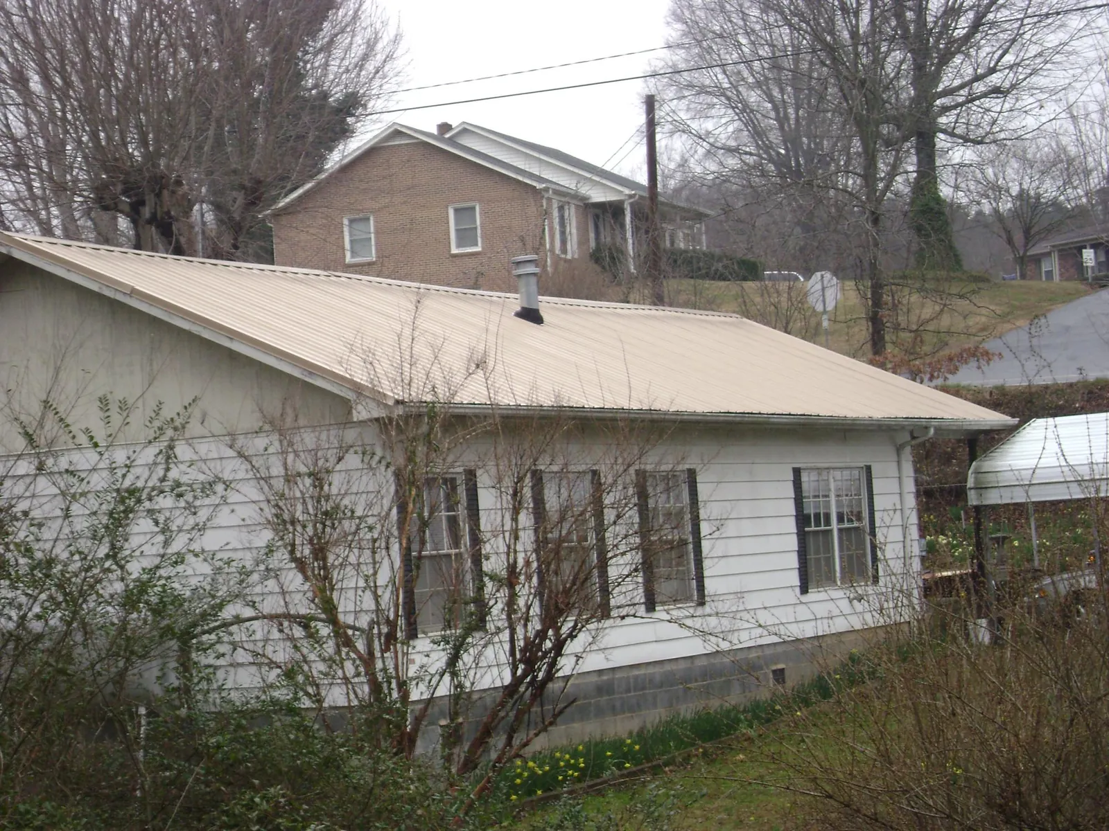 Tan metal roof on a white sided house set into a hillside — Commercial Roofing by Roofing Brothers in Dixon Springs