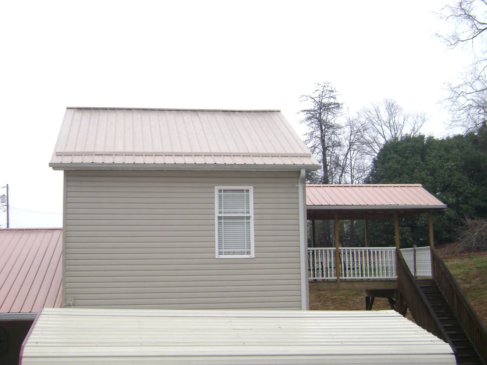 Tan metal roofs on a two story addition and attached porch, from a Roof Replacement job in Dixon Springs